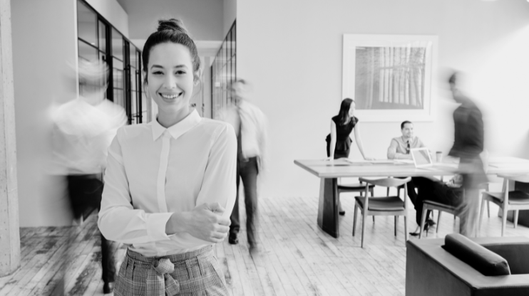 Woman smiling in an office with people at work behind her.